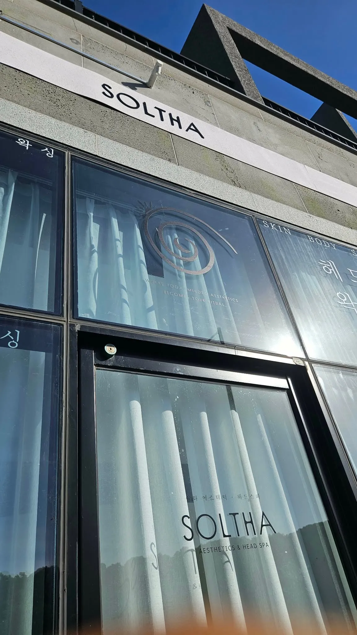 The SOLTHA studio in Jeju Global Education City — the spiral on the glass, sheer curtains behind