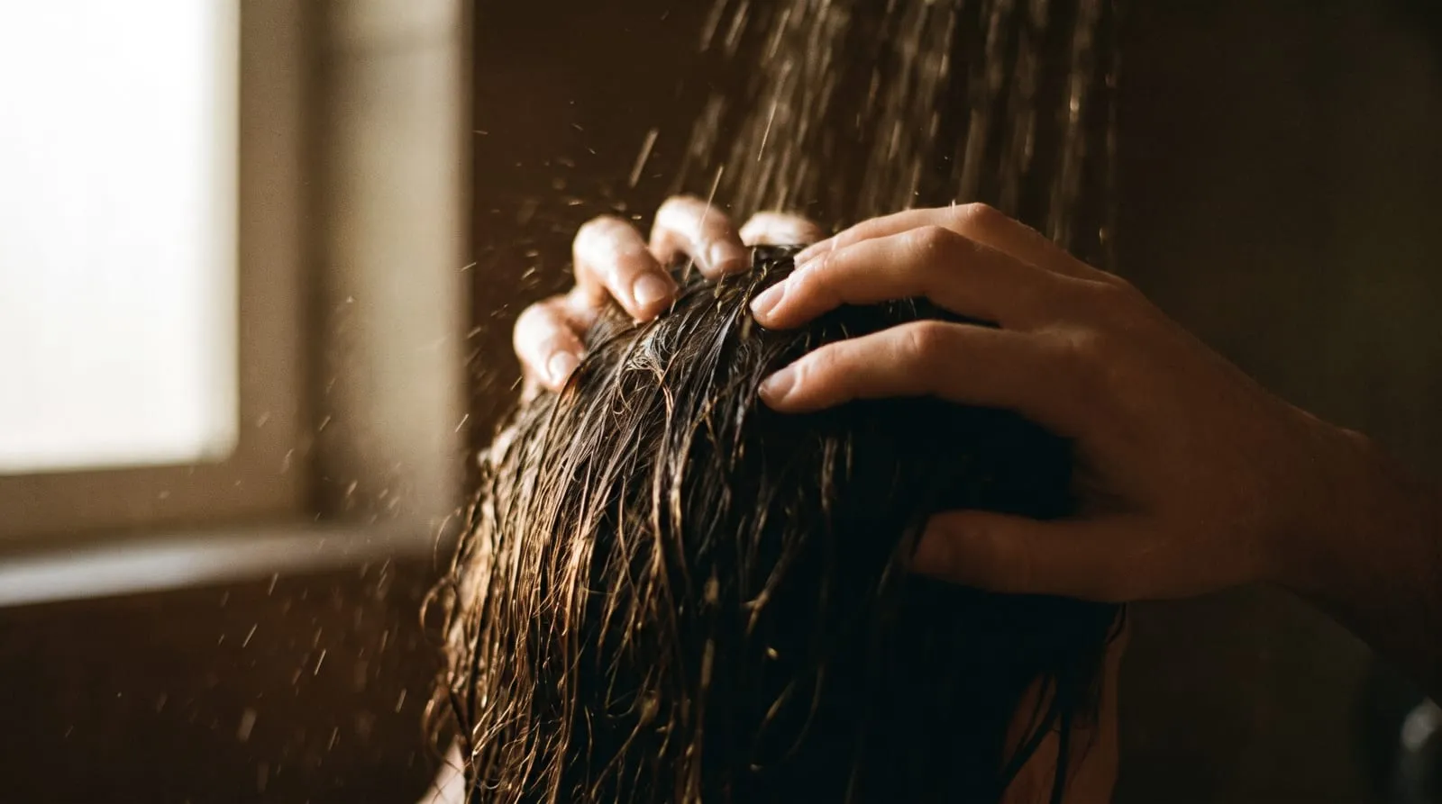 Warm water running through hair at the crown, fingertips working the scalp